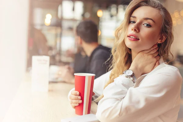 女人坐在咖啡厅里喝她的热咖啡 时尚的微笑的女人在冬季衣服的肖像喝热咖啡 女性冬季风格 图片仅供参考 — 图库照片