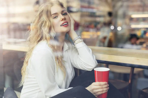 女人坐在咖啡厅里喝她的热咖啡 时尚的微笑的女人在冬季衣服的肖像喝热咖啡 女性冬季风格 图片仅供参考 — 图库照片