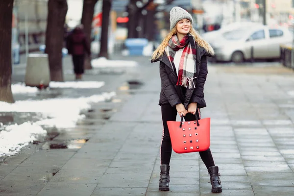 女性は 彼女の赤いバッグを押しながら通りを歩いてします 冬服袋を保持でスタイリッシュな笑顔の女性の肖像画 女性の冬のスタイル イメージ — ストック写真