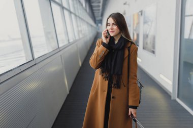 El bagajı tren istasyonu veya yatılı okula gidiş Havalimanı ile yürürken smartphone üzerinde konuşurken Havaalanı iş kadını. Cep telefonuyla konuşma için kız.