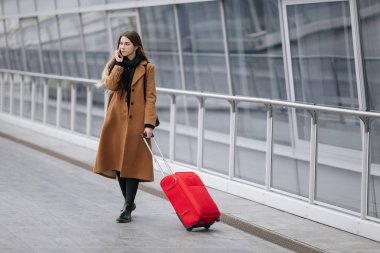 El bagajı tren istasyonu veya yatılı okula gidiş Havalimanı ile yürürken smartphone üzerinde konuşurken Havaalanı iş kadını. Cep telefonuyla konuşma için kız.