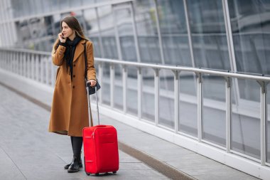 El bagajı tren istasyonu veya yatılı okula gidiş Havalimanı ile yürürken smartphone üzerinde konuşurken Havaalanı iş kadını. Cep telefonuyla konuşma için kız.