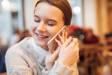 Mutlu kız kafede oturup, mutlu yüz telefonla konuşmak. Beyaz kazak giymek. Kış, sonbahar kıyafeti.