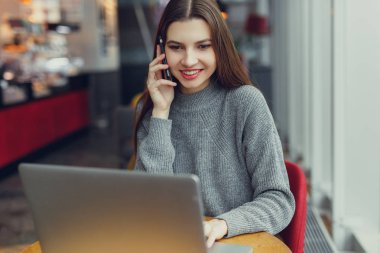 Görünüm. Oturan genç iş kadını masa ve onun telefon laptop bakarken konuşmak. Café'de çalışan kadın. Blogger. -Görüntü