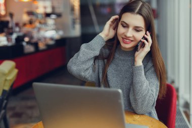 Görünüm. Oturan genç iş kadını masa ve onun telefon laptop bakarken konuşmak. Café'de çalışan kadın. Blogger. -Görüntü