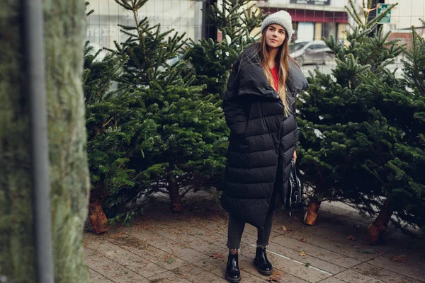 漂亮的女孩穿黑色 寻找完美的圣诞树买在树店 女孩用手检查质量 复制空间 — 图库照片