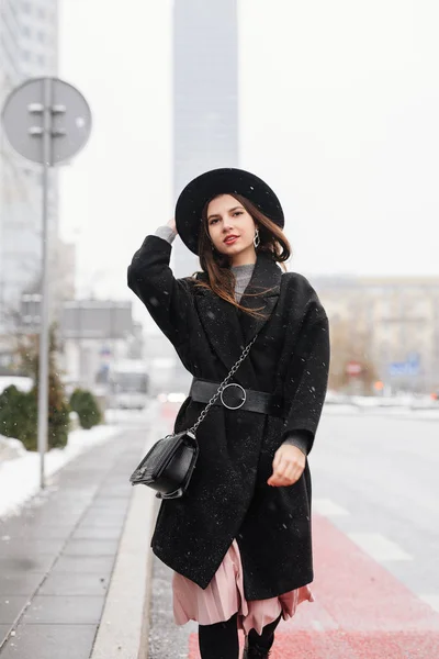 走在城市街道上的年轻时尚女性戴着黑色的帽子环顾四周 对着镜头微笑 复制空间 图片仅供参考 — 图库照片
