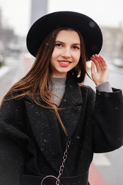 走在城市街道上的年轻时尚女性戴着黑色的帽子环顾四周 对着镜头微笑 复制空间 图片仅供参考 — 图库照片