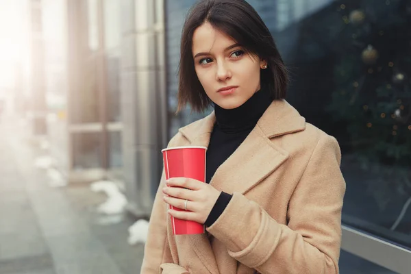 女人在街上散步时喝她的热咖啡 时尚的微笑的女人在冬季衣服的肖像喝热咖啡 女性冬季风格 图片仅供参考 — 图库照片