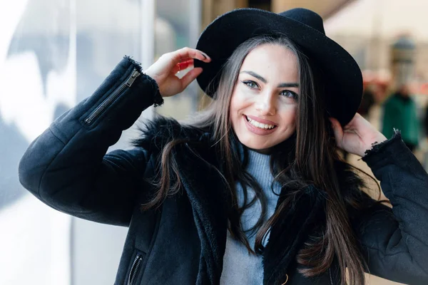 Pretty girl stand on the street wear black hat, look at window store and make funny expressions on her face. - Image