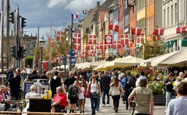 Kopenhag, Danimarka - 24 Temmuz 2023: Ziyaretçiler renkli evleri ve klasik tekneleriyle nyhavn ünlü limanında yürüyorlar