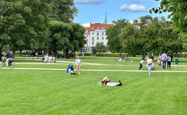 Kopenhag, Danimarka - 25 Temmuz 2023: ünlü Rosenborg şatosu etrafını çevreleyen güzel yeşil parkla birlikte insanlar eski kasabanın yakınında eğleniyor.