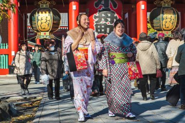 Tokyo, Japonya - 26 Kasım 2012: Renkli geleneksel kıyafetler giyen iki kadın, canlı tapınak alanının önünden geçerken Asakusa 'da gezintiden keyif alıyor.