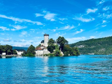 Duingt, Fransa - Eylül 06 2024: Berrak mavi sulara yansıyan tarihi şato, Annecy 'de yemyeşil ve canlı bir gökyüzü altında serin bir gökyüzü oluşturan küçük bir adada duruyor.