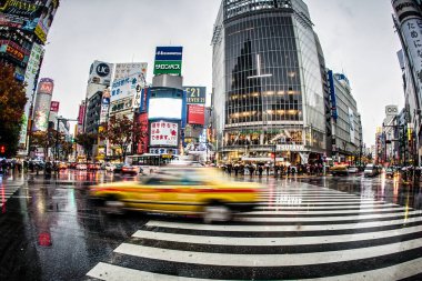 Tokyo, Japonya - 25 Kasım 2012: Yağmurlu hava, Shibuya geçidini çevik yayalar ve neon reklamları arasında sarı taksilerin dolaştığı yer olarak kaplıyor.