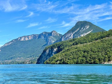 Menthon St. Bernard, Fransa - Eylül 06 2024: Annecy 'de sakin bir göl muhteşem dağ manzaraları ve yemyeşil alanlar sergiliyor. Açık mavi gökyüzü suyu yansıtır ve sakin bir atmosfer yaratır..