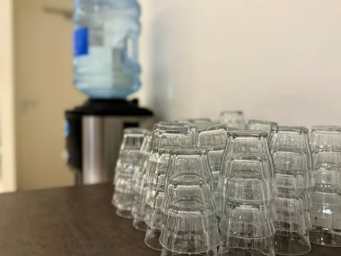 Hollanda, Hollanda, 26 Kasım 2024: Yeniden kullanılabilir cam bardaklardan oluşan bir koleksiyon bir su soğutucusunun yanındaki ahşap bir masaya güzelce istiflenmiştir..