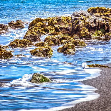 Hawaii, ABD - 07 Eylül 2012: Büyük Hawaii adasında dalgalar pürüzsüz kayaların üzerinde yuvarlanıyor parlak bir gökyüzü altında sakin bir kıyı atmosferi yaratıyor.