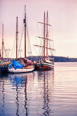 Oslo, Norveç - 25 Nisan 2012: Sükûnet dolu bir akşamda gökyüzünün canlı renklerini yansıtan renkli tekneler Oslo limanında huzur içinde dinleniyor.