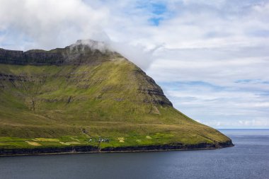 Atlantik Okyanusu 'na ulaşan yüksek dağlar Faroe Adaları' nın manzarası için tipik bir özelliktir. Birkaç ev sınırda duruyor..