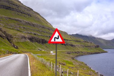 S virajından önce trafik işareti. Faroe Adaları 'nda tipik bir durum. Dağların altından fiyortların üzerinden bir yol esiyor..
