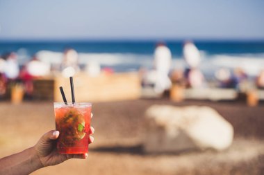 El ile güneşli sahil arka plan üzerinde çilek mojito tutuyorsun.
