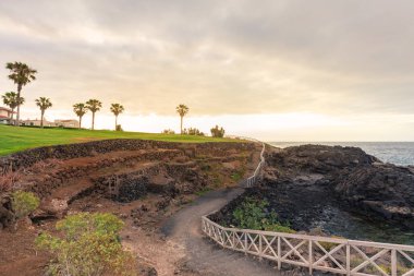 Toprak yol kayalık sahil şeridi boyunca küpeşte ile.