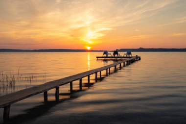 Gölde gündoğumu sırasında ahşap iskele üzerinde üç boş koltukları.