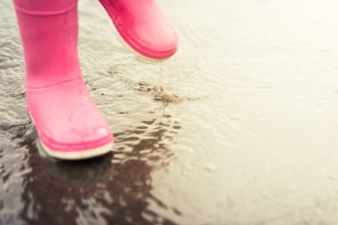 Atlama ve su birikintisi üzerinde yağmur sonrası sıçramasına pembe lastik Çizmeli çocuk metrelik.