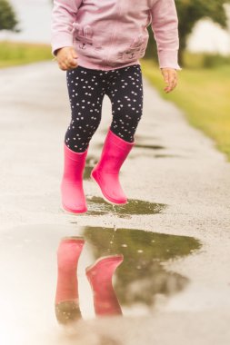 Atlama ve su birikintisi üzerinde yağmur sonrası sıçramasına pembe lastik Çizmeli çocuk metrelik.