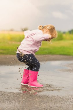 Su birikintisine oynama ve sıçramasına küçük kız onu wellies su.