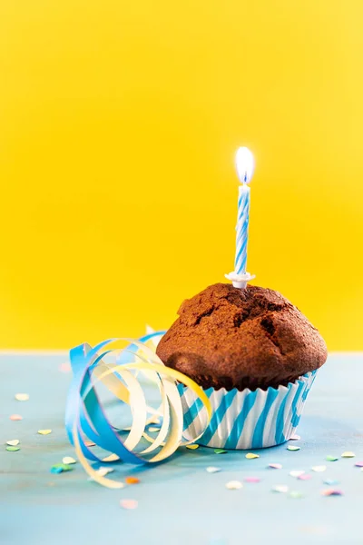 Birthday cupcake with single candle on blue and yellow background.