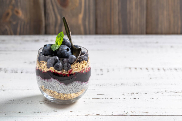 Light dessert of chia pudding with blueberry, oats and fresh jam, served in thin glass. 