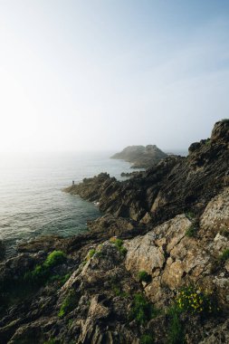 Alacakaranlıkta kayalıklarda duran yalnız balıkçı. Pointe du Grouin in in Bretagne.