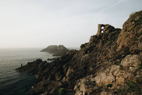 Alacakaranlıkta kayalıklarda duran yalnız balıkçı. Pointe du Grouin in in Bretagne.