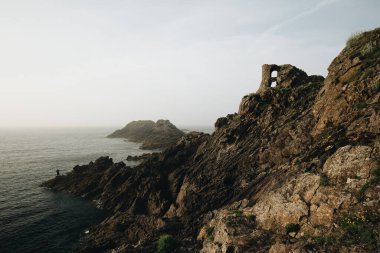 Alacakaranlıkta kayalıklarda duran yalnız balıkçı. Pointe du Grouin in in Bretagne.