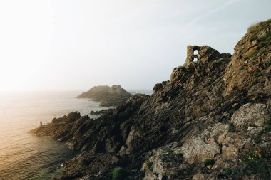 Alacakaranlıkta kayalıklarda duran yalnız balıkçı. Pointe du Grouin in in Bretagne.