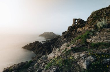 Alacakaranlıkta kayalıklarda duran yalnız balıkçı. Pointe du Grouin in in Bretagne.
