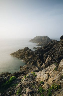 Alacakaranlıkta kayalıklarda duran yalnız balıkçı. Pointe du Grouin in in Bretagne.
