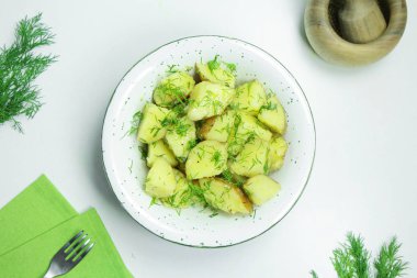 Taze dereotu ve beyaz bir arka plan üzerinde beyaz bir kasede yağ ile haşlanmış patates