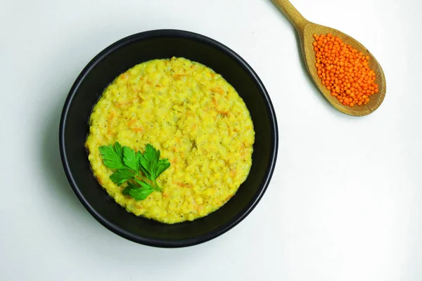 Beyaz bir tablo üzerinde siyah bir kasede maydanoz ile tepesinde sağlıklı mercimek püresi