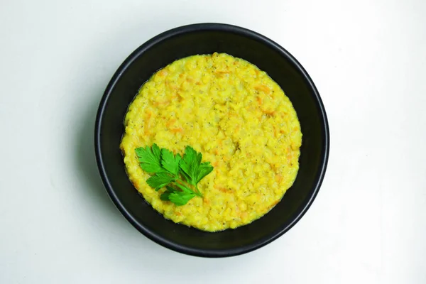 Beyaz bir tablo üzerinde siyah bir kasede maydanoz ile tepesinde sağlıklı mercimek püresi