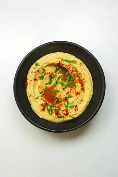 Ev yapımı humus zeytinyağı ve kırmızı beyaz bir arka plan üzerinde siyah bir kase biber ile