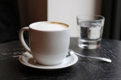 Káva Latte v bílém cup na starý dřevěný stůl se sklenkou vody a lžíce.