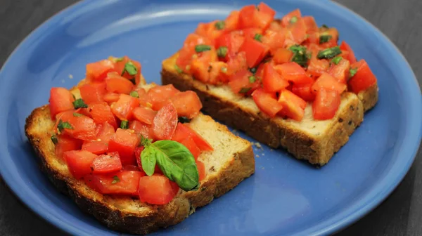 Bruschetta com tomates frescos e manjericão verde em uma chapa azul em um fundo de madeira. Comida italiana saudável . — Fotografia de Stock