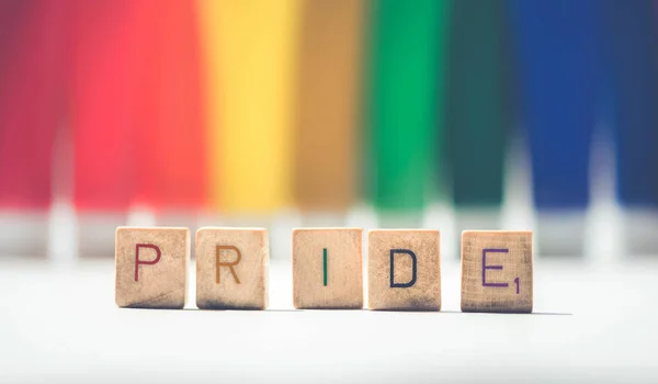 骄傲标志与五颜六色的木制字母字母在骄傲的Lgbt彩虹旗背景. — 图库照片