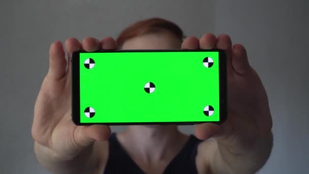 目の前に黒いスマートフォンを垂直に持っている男 緑色の画面またはクロマキーを備えた携帯電話 トラッキングモーションポイントを持つモックアップテンプレート ウード4Kでクローズアップ — ストック動画