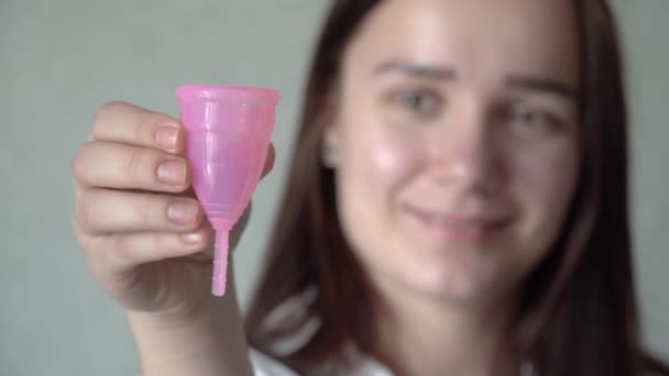 再利用可能なシリコーン月経カップを顔の前に持つ若い女性の手のクローズアップ 廃棄物月経衛生コンセプトをゼロにします 期間の生態学的代替 — ストック動画