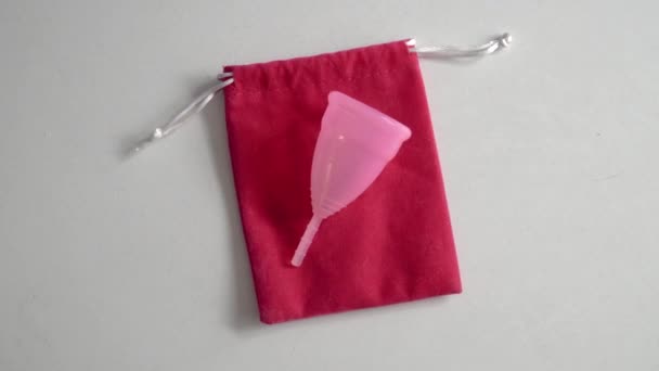 Uzavřete silikonový menstruální šálek, který se nachází na růžovém vaku na bílém stole. Koncept hygieny při menstruaci. Ekologická alternativa pro období.