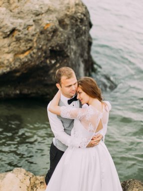 Gülümseyen yeni evliler deniz arasında Uçurumdaki sarılıyorlar. Yukarıdaki romantik portre.